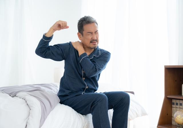 ベッドに腰かけて肩を押さえる男性